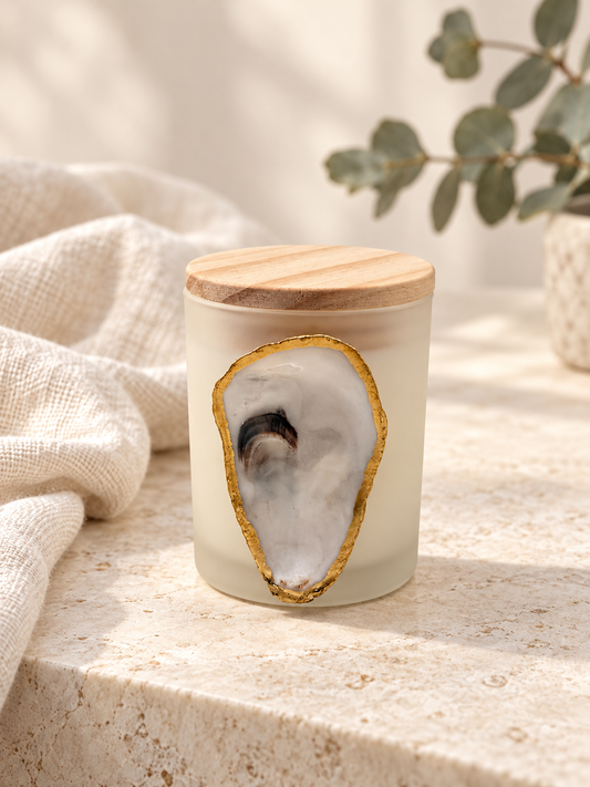 Hand-poured oyster candle in a frosted jar with wooden lid and gold-edged oyster shell